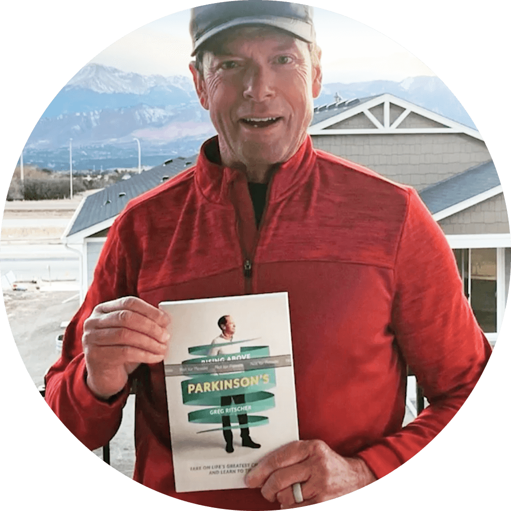 Photo of a 23andMe research participant, Greg, who is holding the book he wrote about Parkinson's.